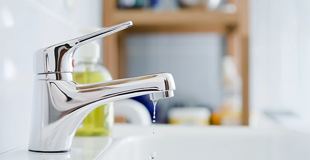 Close-up of a modern chrome faucet with water droplets, set against a softly blurred kitchen background.