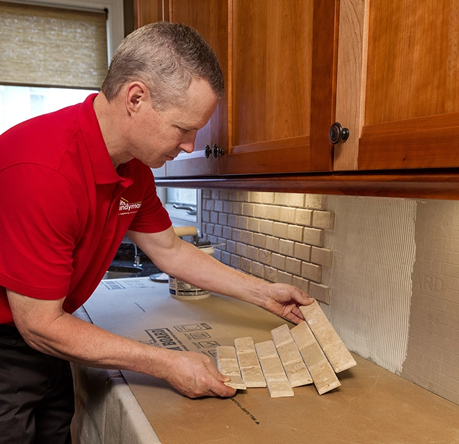 A person arranges tile pieces on a kitchen counter, preparing to install a backsplash near wooden cabinets.