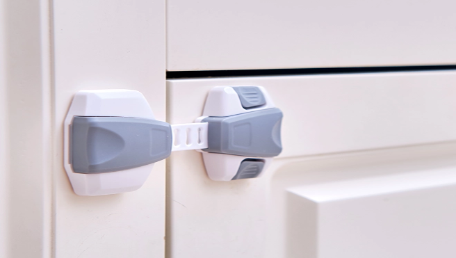 A white and gray cabinet safety lock securing two cabinet doors, preventing them from being opened easily.