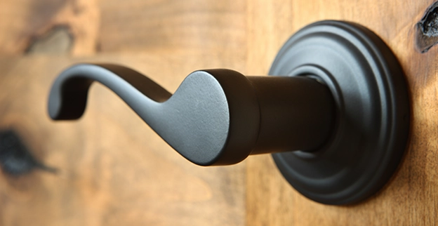 Close up of a black door handle mounted on a textured wooden door.