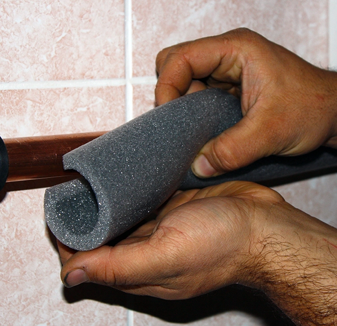 A person fits gray foam insulation around a copper pipe.