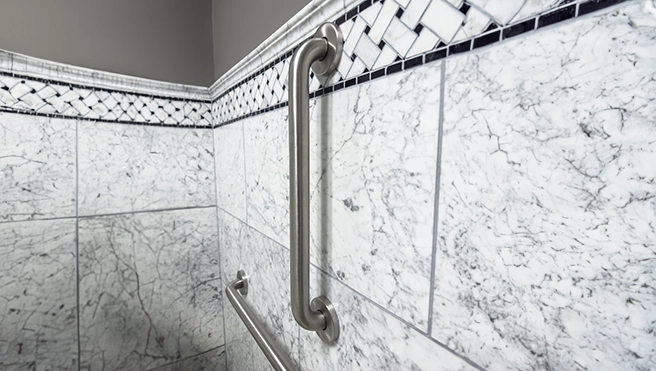 A close-up of a polished metal grab bar mounted on elegant marble shower tiles.