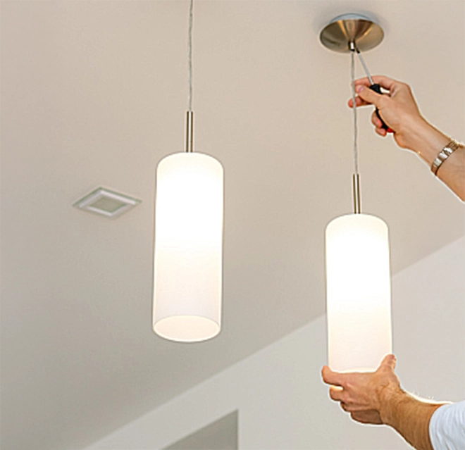 Hanging two modern pendant lights with cylindrical white shades.