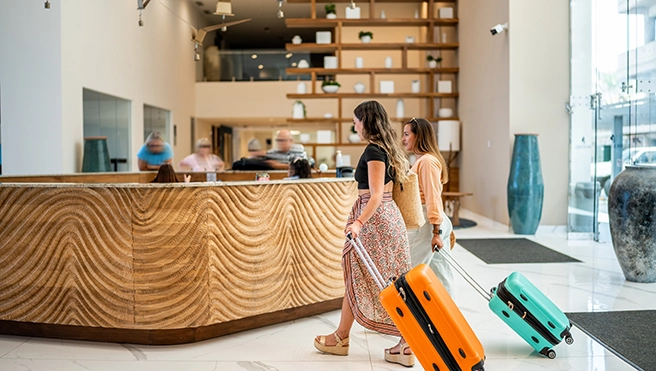 Two women with luggage enter a hotel lobby.