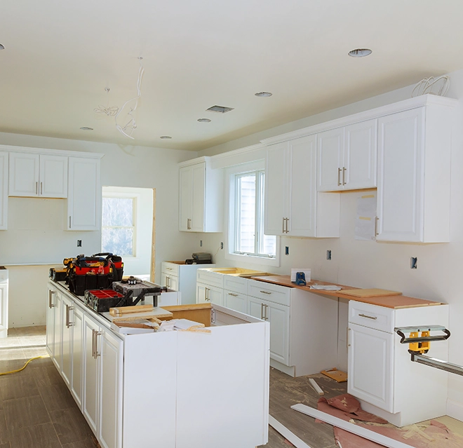 A partially renovated kitchen featuring white cabinetry.