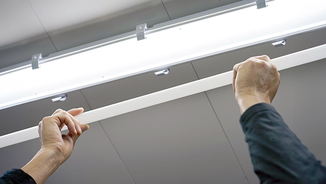 A person installs a white light fixture in a ceiling-mounted fluorescent light setup.