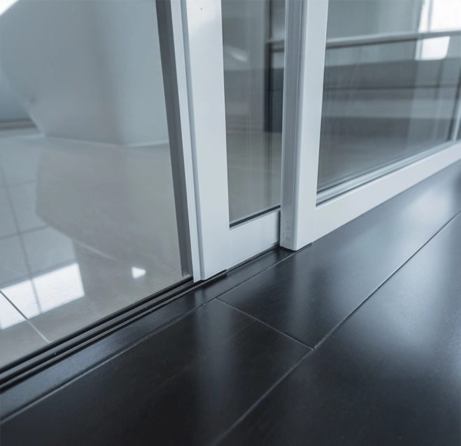 A sliding glass door's track system on dark wooden flooring.
