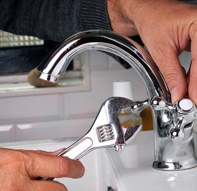 A person using a wrench to repair a chrome kitchen faucet.