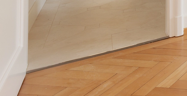 Transition between light-colored tiled flooring and dark wood flooring at a doorway.