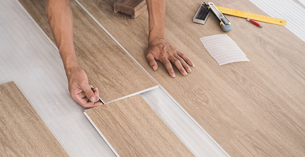 Handyman laying a wooden flooring planks and marking for precise placement with tools.