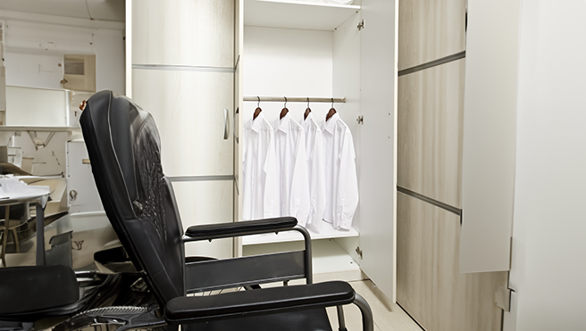 A black chair in a dressing room beside a closet with neatly hung white shirts