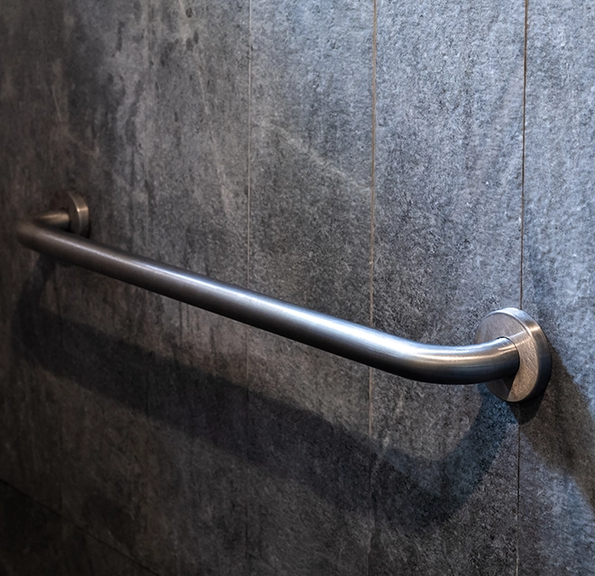 A sleek stainless steel grab bar mounted on a textured gray stone wall.