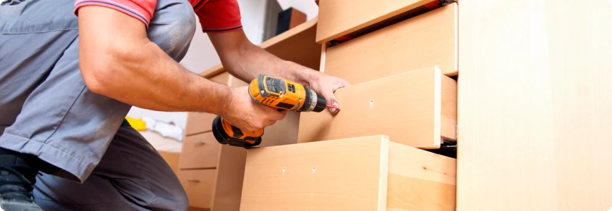 An individual using a drill to assemble drawers on a desk.
