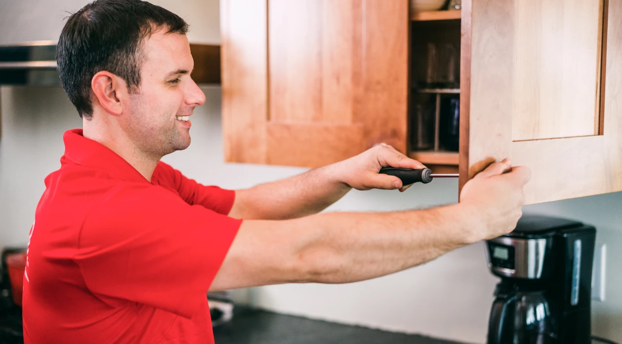 A Mr. Handyman service professional uses a screw driver to assemble a cabinet.