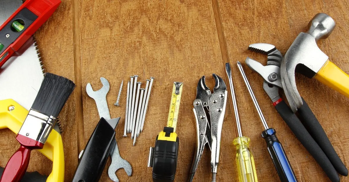 A collection of tools that would commonly be used by a handyman in Longmont, CO, including a hammer, saw, level, tape measure, utility knife, pair of screwdrivers, and several nails.
