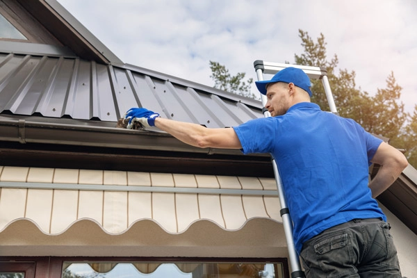 Man standing on ladder cleaning out gutter