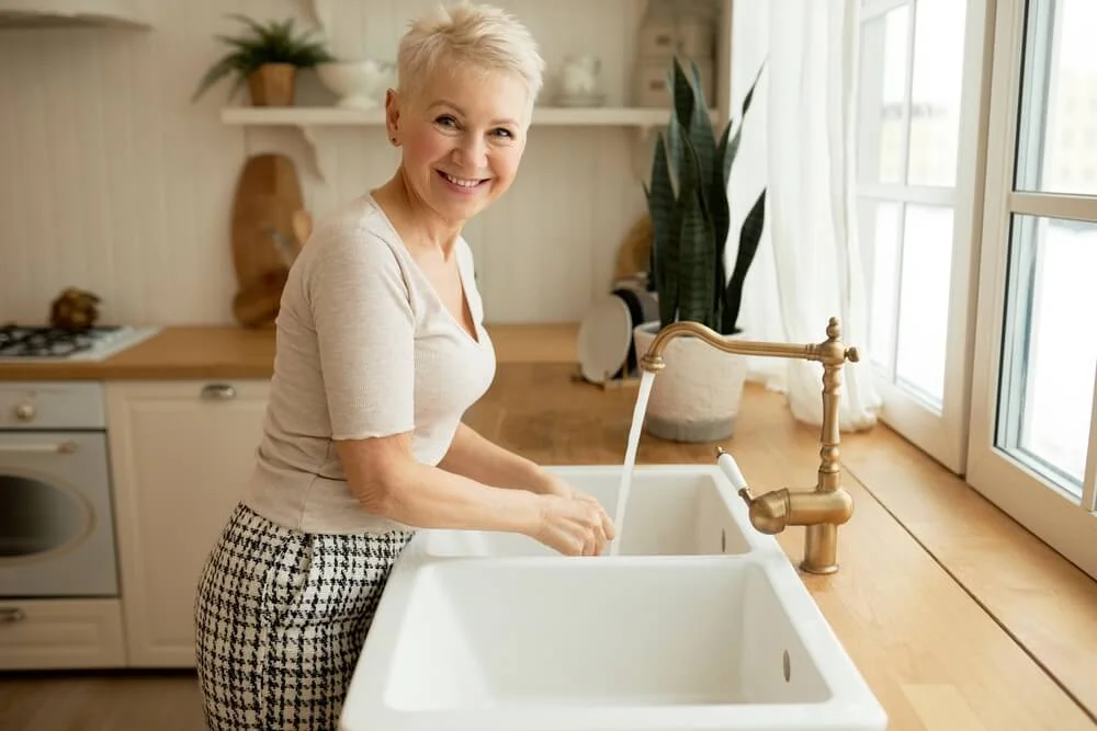 An older woman washing hands in kitchen sink.