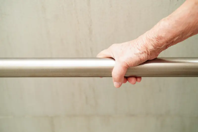 Older adult's hand holding onto a metal grab bar.