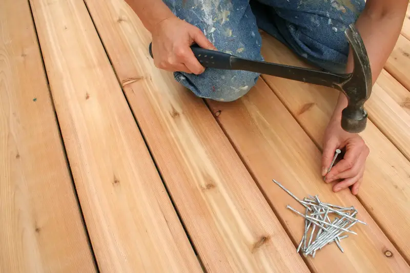 An individual nailing down the boards for a floating deck.