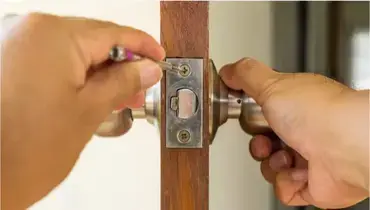 A close-up of the side of a door where a handyman performing door repairs is using a screwdriver to adjust a door latch.