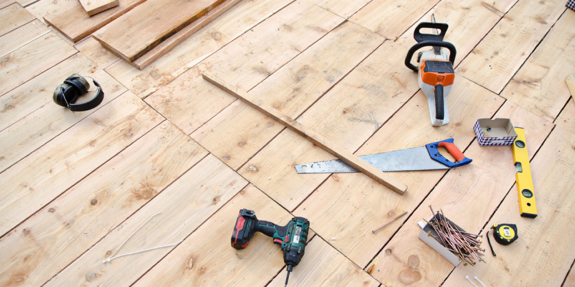 A collection of hand tools, power tools, and safety gear spread across a deck that has recently received deck repairs.
