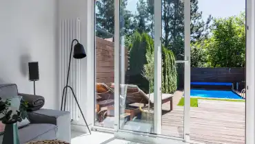 A glass patio door that opens out to a deck with a pool and nearby shrubbery.