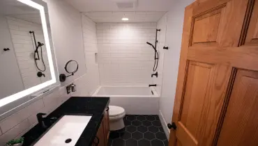 A modern bathroom with a deep bathroom, black hardware, black and white tile, and a solid wood door.