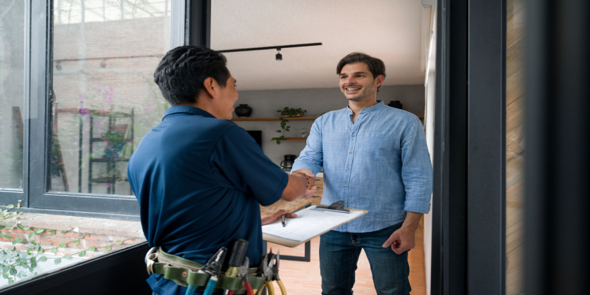 A handyman greeting a homeowner while wearing a tool belt.