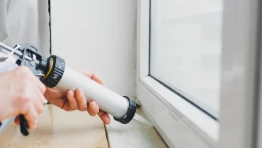 Handyman holding a caulking gun with a tube of caulk as they provide caulking service for a residential window