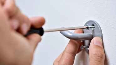 Handyman providing hanging service by using a screwdriver to attach a clothes hook to a wall