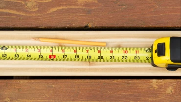 Tape measure and pencil sitting on top of an unpainted, new deck board installed for deck repair