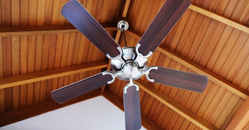 A ceiling fan hanging below the top of a tall, vaulted residential ceiling with visible wood beams.