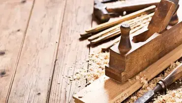 Wood shavings and tools used for carpentry lying on wooden boards, including a plane, chisel, and hammer.