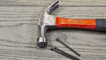 A hammer and screws laying on the worn boards of a porch before being used for porch repair.