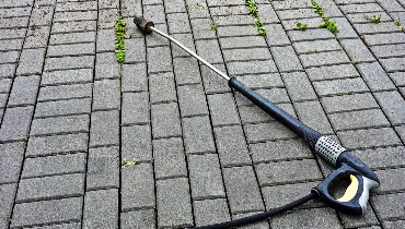 A pressure washing sprayer lying on a stone walkway that has been partially cleaned with pressure washing service.