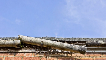 A damaged gutter system filled with roots and debris, with one section entirely broken off, that should be fixed or replaced with professional gutter repairs.