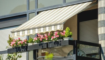 An awning extended over flowers on the balcony of a home that has just received awning installation service.