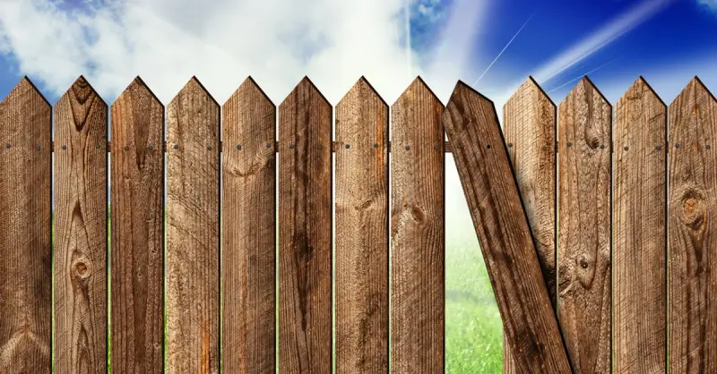 A wooden fence with a crooked picket that should be fixed with professional service for fence repairs.