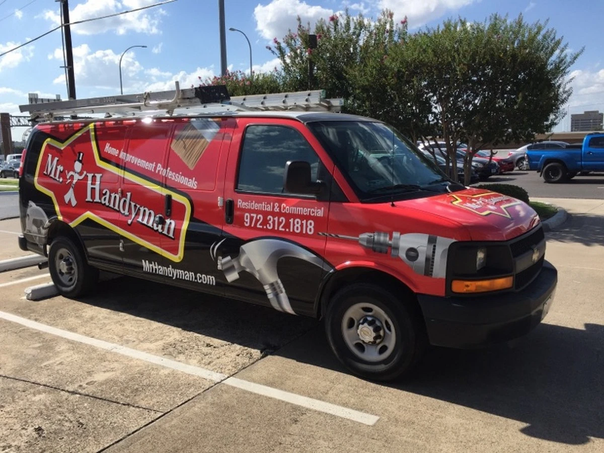 A work van with ladders on top that has been branded with the Mr. Handyman logo and an image of a hammer and drill.