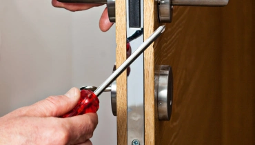 A handyman using a screwdriver to repair the locking mechanism of a door during an appointment for door repairs.