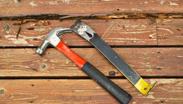 A hammer and pry bar lying on a weathered deck before being used to complete deck repairs.