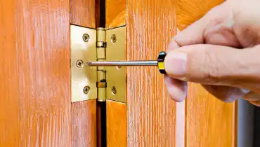 A handyman using a screwdriver to adjust a door hinge during an appointment for door replacement.