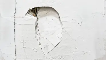A large hole and many cracks in a residential wall that will require major drywall repair services to fix.