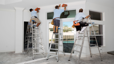 Professional technicians stand on ladders while installing crown molding.