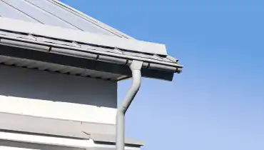 A new gutter and downspout attached to the corner of a roof with gutter installation service.