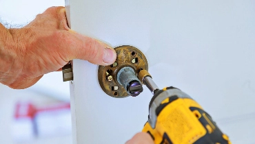 A handyman using a drill to change the lock on a door while providing door repair services.