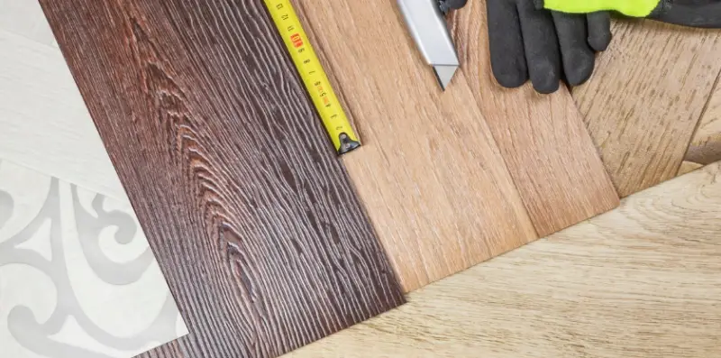 Samples of materials used for flooring repair spread out across a floor with a tape measure, box cutter, and a pair of work gloves.