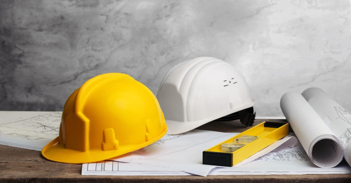 Two hardhats, a level, and several diagrams for renovation plans laid out on a table for use by a general contractor in Dallas, TX.
