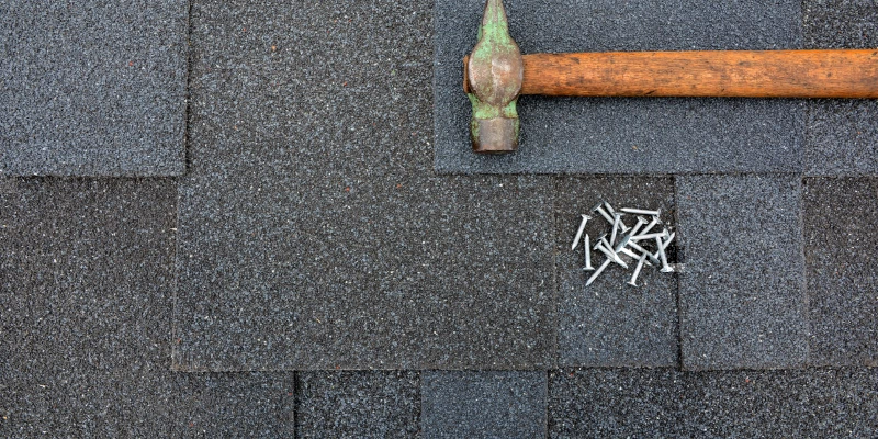 A hammer and nails lying on top of a roof after new shingles have been installed during an appointment for roof repair.