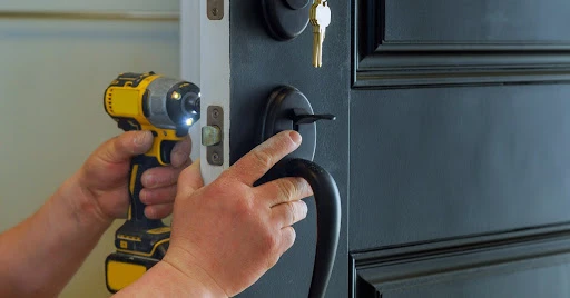 Hands holding a handheld power drill as it’s being used to complete repairs for the lock on an exterior residential door.